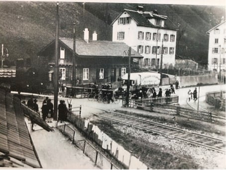 FussängerInnen, Velos, und ein Lastwagen warten an der Barriere neben dem Wärterhäuschen, bis die aus dem Zimmereggtunnel brausende Dampflok ihres Weges gezogen ist. Bild vor 1929. Quelle: SALU N1.05.45